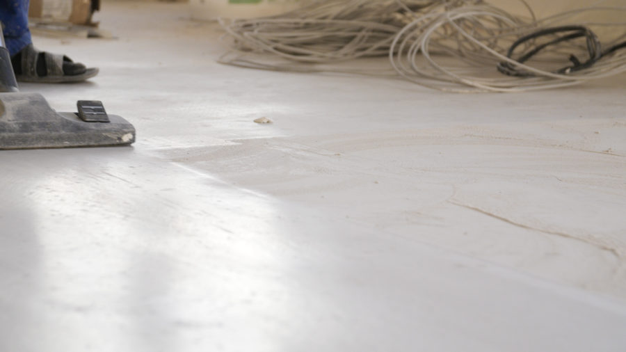 Workers in uniform cleaning room with a vacuum cleaner after installing wood parquet board during flooring work. Man vacuuming floor during repairs.