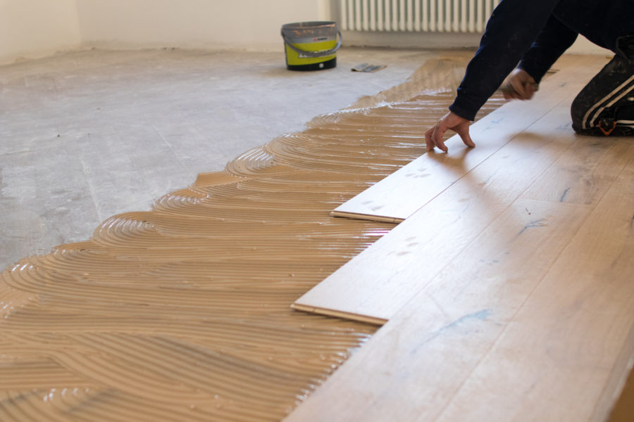 Renovation of an apartment, skilled worker uses a plastic hammer when installing pre-finished interlocking parquet. Laying with brown glue on an existing floor. Installation of oak colored parquet